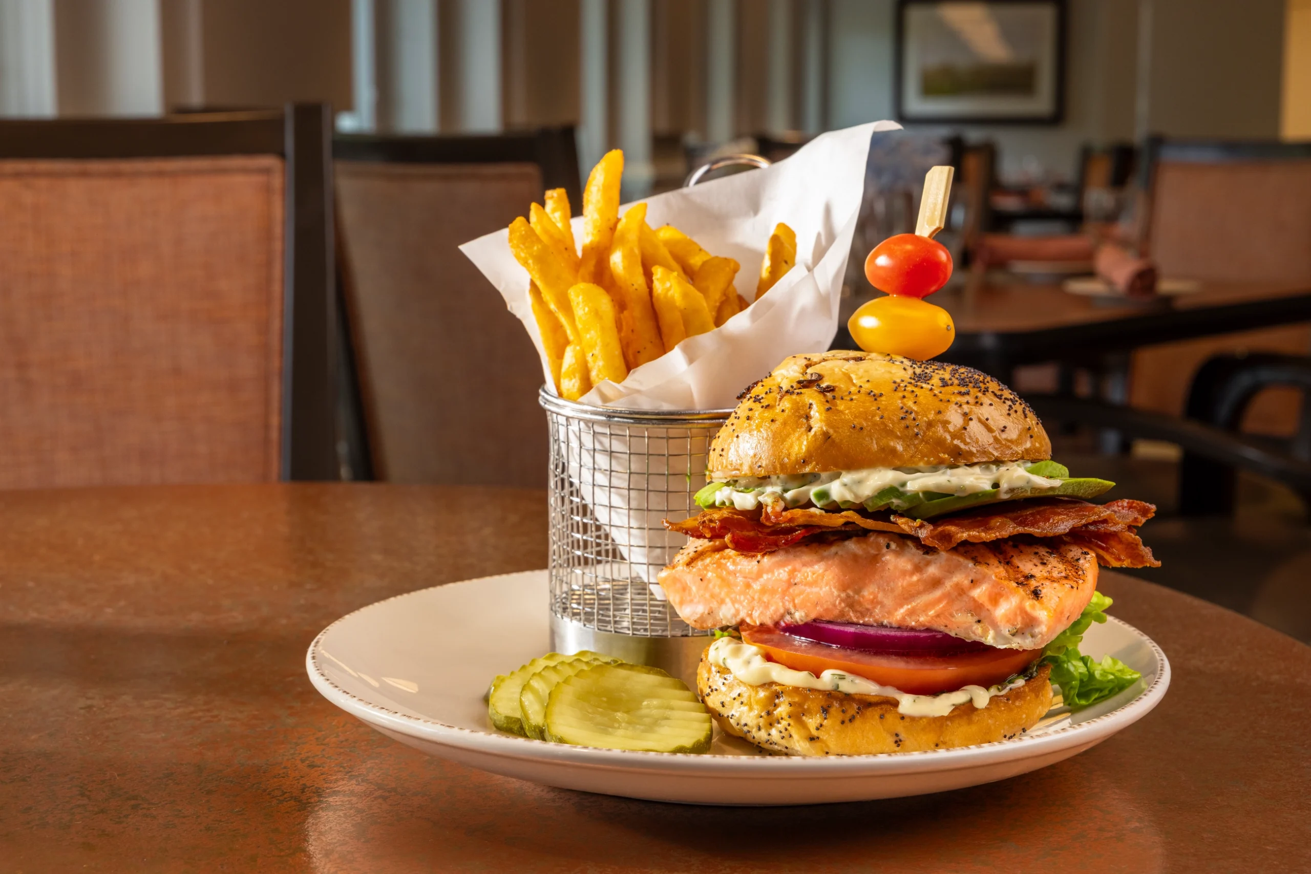 A grilled salmon burger with bacon, avocado, lettuce and herb aioli on a poppy seed bun, served with a basket of fries