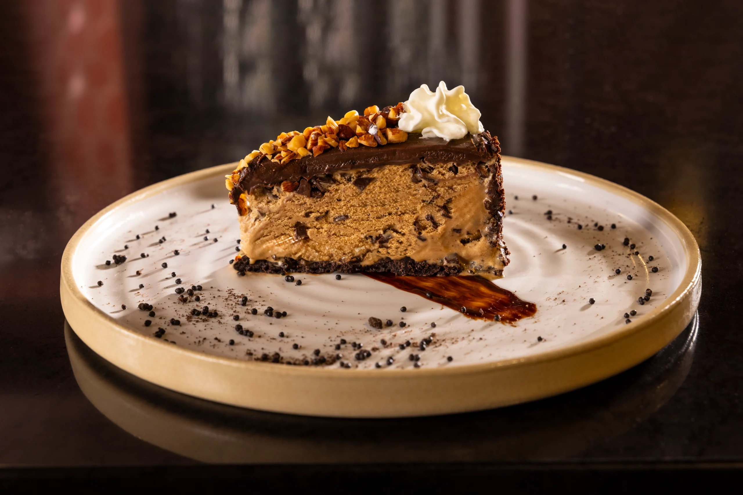 A slice of frozen mocha ice cream cake with chocolate ganache, chopped hazelnuts and whipped cream