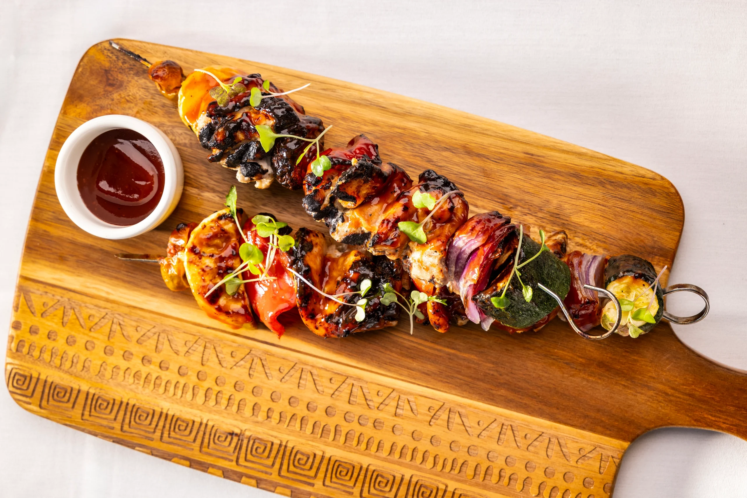 Grilled chicken and vegetable skewers glazed with barbecue sauce, served on a carved wooden board