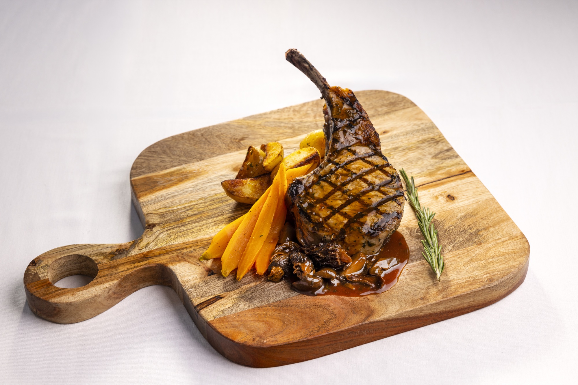 A grilled bone-in pork chop with roasted potatoes and glazed carrots